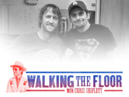 Two men smiling in a recording studio with posters visible on the wall.