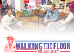 Three people seated in a recording studio discussing music among colorful posters.