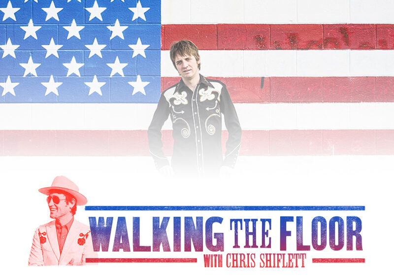 Man in ornate embroidered vest standing before an American flag.