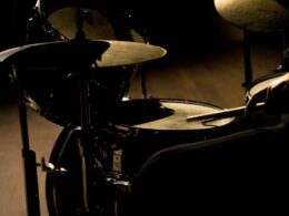 Drum kit with multiple cymbals lit by dramatic side lighting.