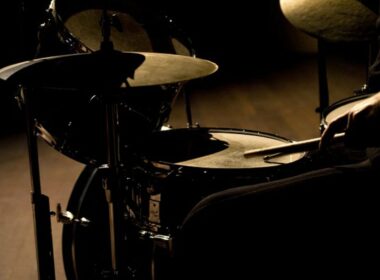 Drum kit with multiple cymbals lit by dramatic side lighting.
