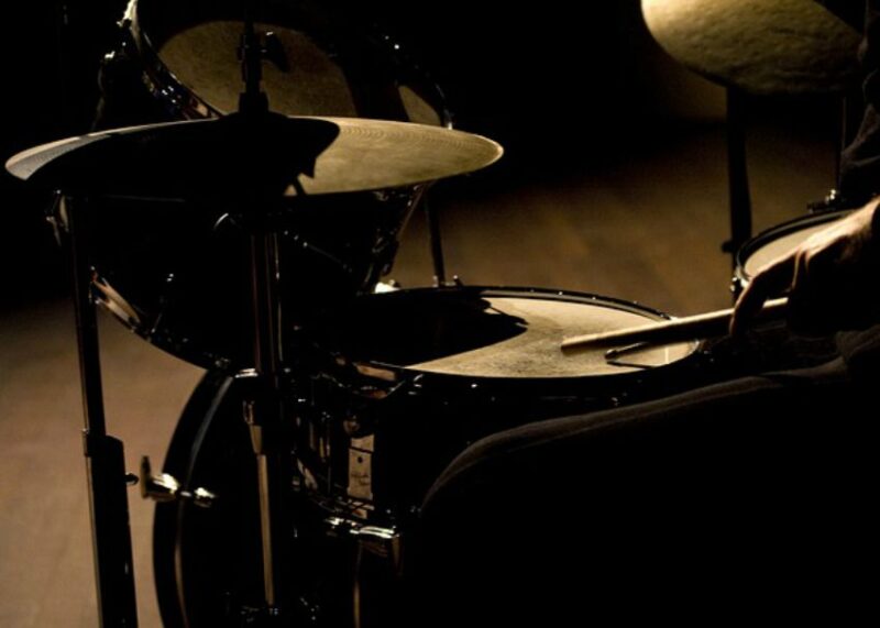 Drum kit with multiple cymbals lit by dramatic side lighting.