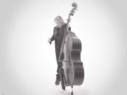 A musician with long hair plays a cello against a white background.