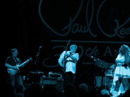 Band performing on stage in blue lighting with guitarists, drummer, and singer.