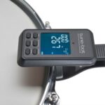 Black digital drum tuner with blue LCD display mounted on a drum.