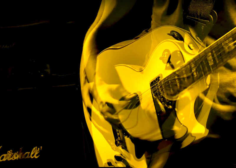 Yellow electric guitar played during performance, captured in warm stage lighting.