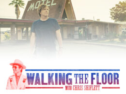 Man in blue shirt stands outside rundown motel for Walking the Floor promotion.