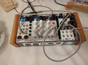 A Moog synthesizer with wooden frame and blue LED displays sits on a white surface.