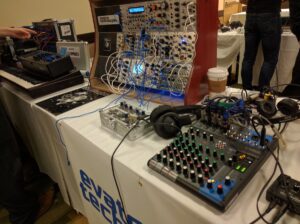 Event synthesizer display with Yamaha mixer, blue cables, wooden modules, keyboard, and equipment.