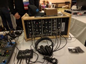 Wooden frame synthesizer system displayed on event table with additional modules and cables.
