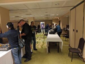 Convention floor with multiple attendees viewing various synthesizer booths and musical instrument displays.