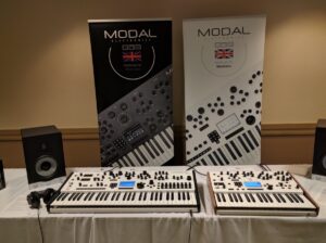 Two Modal Electronics synthesizers sit on display with promotional banners showcasing the brand and equipment.