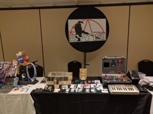 The SMSI booth displays synthesizer keyboards and modular equipment with promotional signage hanging above.