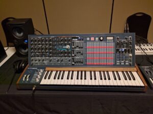 An Arturia synthesizer with orange accent on desk next to speakers and headphones.