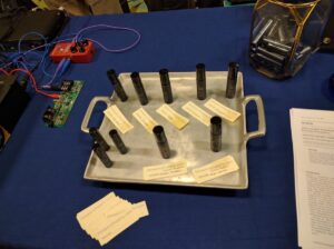 Metal trays hold cylindrical electronic components, circuit modules, and blue connector cables on a blue work surface.