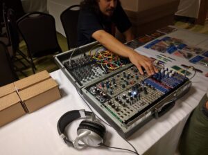 A person works with synthesizer modules, colorful wiring, and electronic components inside a flight case equipment setup.
