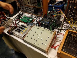 Multiple modular synthesizer modules and circuit boards with colorful wiring cables are displayed on a table.