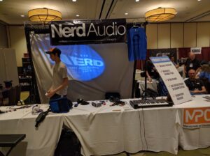 A Nerd Audio booth features a keyboard synthesizer with a large projection display and overhead lighting.