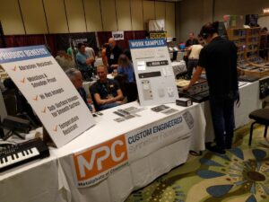 Attendees browse electronic music equipment booths at a convention featuring synthesizers and audio gear displays.