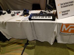 A black keyboard synthesizer sits on a white table with scattered electronic components nearby.