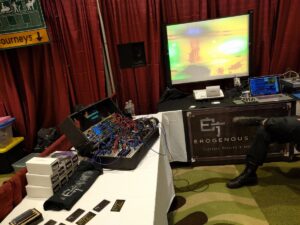 A synthesizer with blue wiring displays thermal imaging visuals on a large projection screen.
