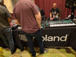 Person at Roland booth examines a large synthesizer with integrated circuit boards and keyboard.