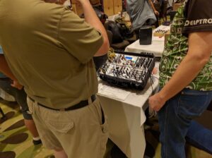 Two people examine an open equipment case with a patch bay containing numerous colorful cables.