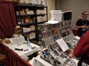 Electronic music equipment booth displays circuit boards, boxed modules, and a presenter standing nearby.