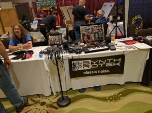 A man demonstrates vintage synthesizers at a Classic Noise booth with modular patching systems.