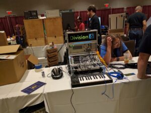 A man wearing headphones works at a Division 6 synthesizer booth with modular equipment.
