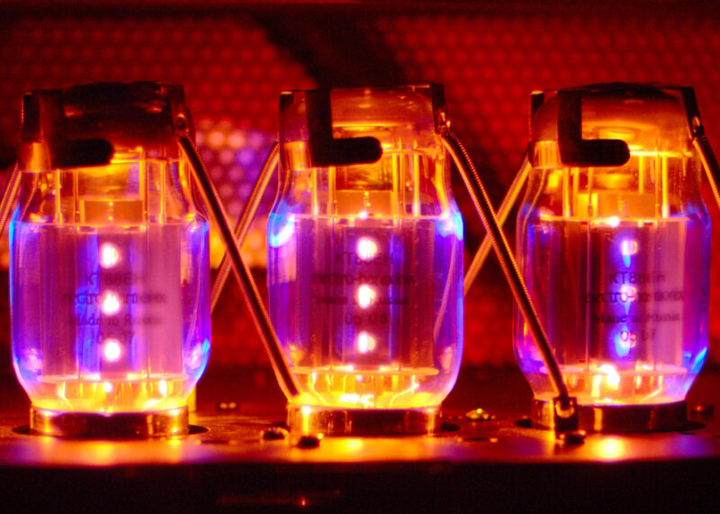 Three vacuum tubes glow with blue and orange light against a red background.