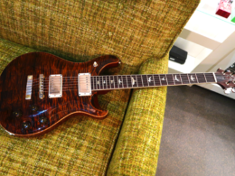 A dark burgundy semi-hollow body electric guitar placed on a textured green couch.