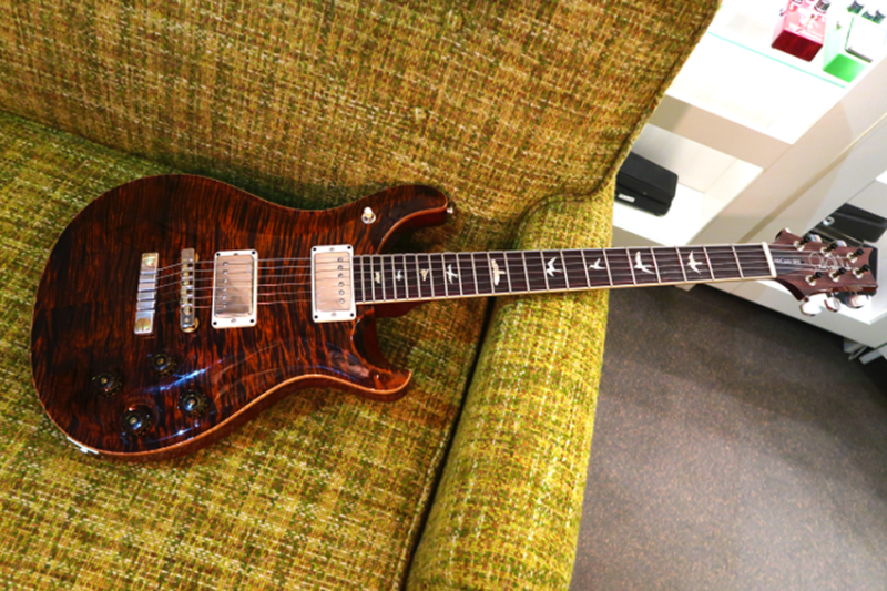 A dark burgundy semi-hollow body electric guitar placed on a textured green couch.