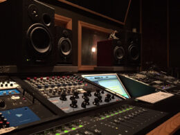 Professional recording studio control room featuring a large mixing console, monitors, and sophisticated audio equipment.
