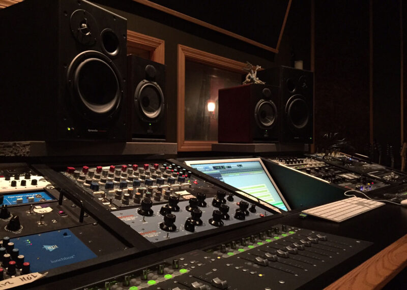 Professional recording studio control room featuring a large mixing console, monitors, and sophisticated audio equipment.