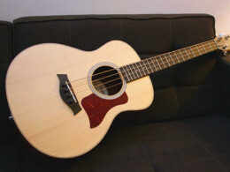 A light wood acoustic bass guitar rests on a dark couch.