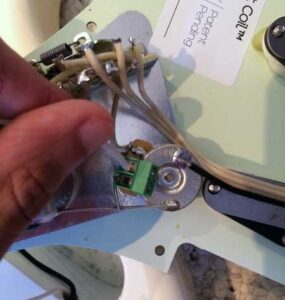 A hand holds a jack lead terminal assembly with brown wires soldered to a green circuit board component.