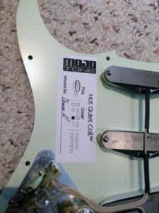 White Mojo Tone pickguard held with product label and documentation visible.