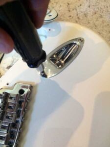 Hand removing a chrome output jack connector from the white guitar pickguard.