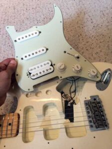 White Stratocaster pickguard held up showing three single-coil pickups with wiring.