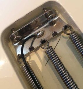 A tremolo assembly features a metal cavity, springs, and soldered connections for a guitar tremolo system.