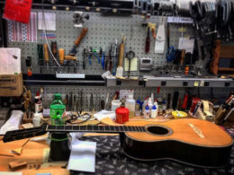 A luthier uses a metal straightedge tool to dress and align guitar frets.