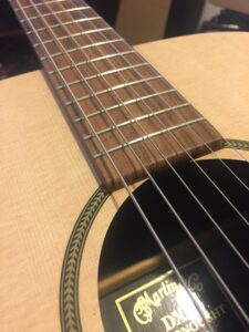 A guitar neck displays fresh metal strings aligned across wooden frets.