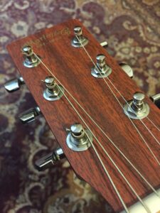 Close-up of wooden guitar headstock with new strings installed through metal tuning pegs.
