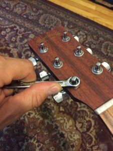 Close-up of guitar headstock tuning pegs being tightened with a wrench.