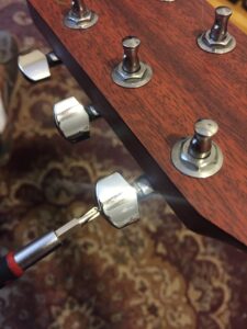 Close-up of guitar headstock with metal tuning pegs being adjusted by a screwdriver.