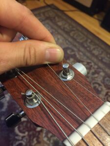 A hand plucking an unwound plain guitar string on a wooden headstock.