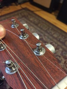 A hand adjusts unwound plain strings around chrome tuning pegs.