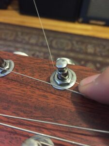 An unwound plain guitar string extends from a metal bridge pin.