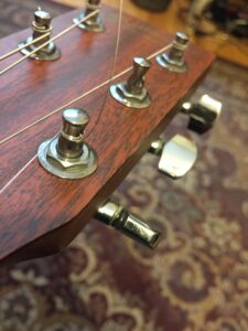 Unwound plain guitar strings route across tuning pegs on a wooden headstock.